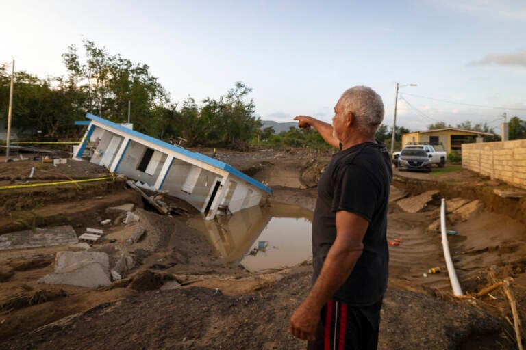 A man gestures towards a building sunk into mud.