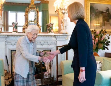 Queen Elizabeth, facing the camera, shakes the hand of Liz Truss, who is faced away from the camera.