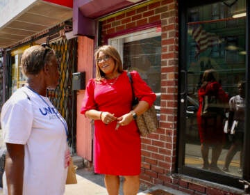 A woman in a red dress talks to another person outside of a brick building.