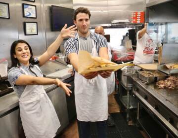 Gianna Yanelli (left), who portrays Adrian in Walnut Street Theatre’s production of ‘’Rocky, the Musical,’’ and Matthew Amira, who portrays Rocky, make cheesesteaks at Pat’s King of Steaks in South Philadelphia. (Emma Lee/WHYY)