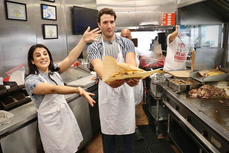 Gianna Yanelli (left), who portrays Adrian in Walnut Street Theatre’s production of ‘’Rocky, the Musical,’’ and Matthew Amira, who portrays Rocky, make cheesesteaks at Pat’s King of Steaks in South Philadelphia. (Emma Lee/WHYY)
