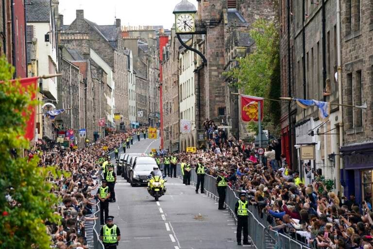 A hearse makes its way through the street in Scotland, which is lined with people on either side.