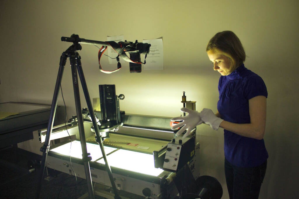 A woman pulls on a plastic glove in a dimly lit room with a scanning machine.