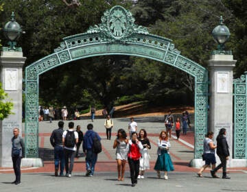 Students walk through a green arch on a college campus.