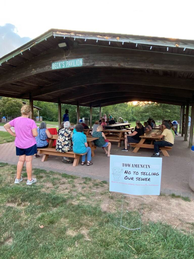 A group of people gather under an outdoor pavilion.