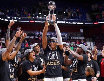 A basketball player holds up a trophy as her teammates surround her to celebrate.