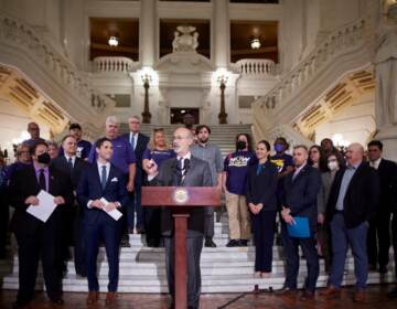 Gov. Wolf speaks at a podium surrounded by elected officials and others.