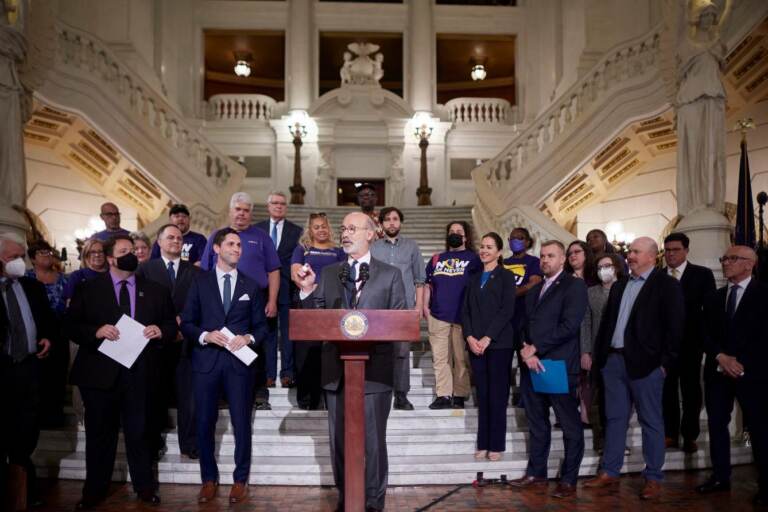 Gov. Wolf speaks at a podium surrounded by elected officials and others.