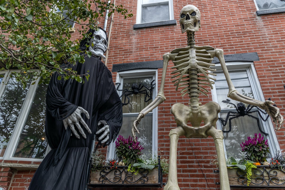 A towering grim reaper and skeleton stand on a Philly street