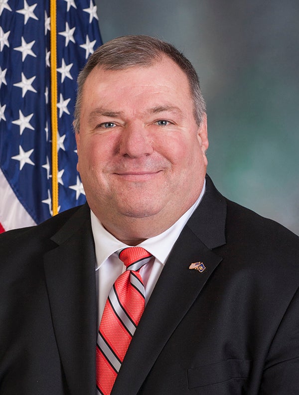 A man smiles and poses for a photo wearing a suit and tie.