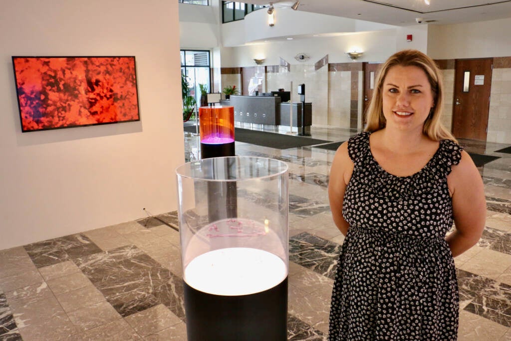 A woman stands next to a display case in a gallery.