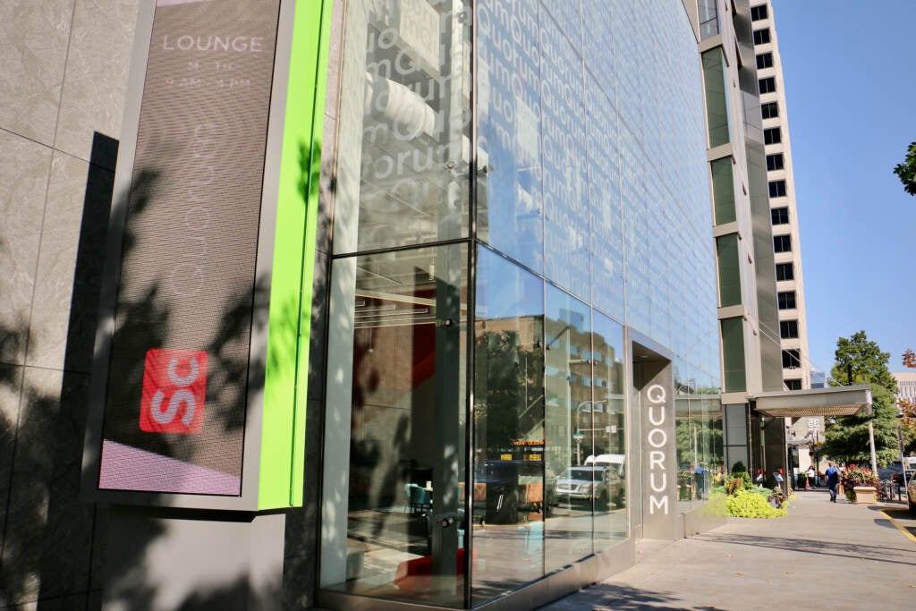 A tall glass building with the name Quorum written near the door is visible to the left of a sidewalk.