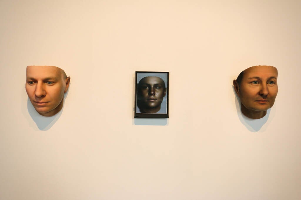 Three images of a person's face are displayed on a wall.