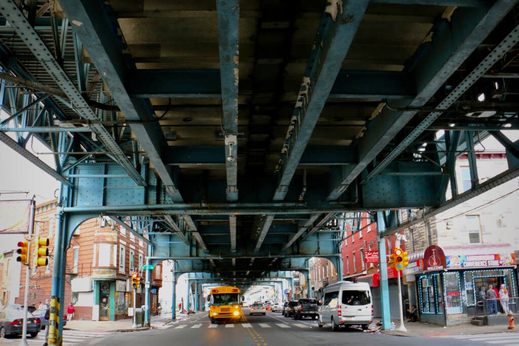 Cars drive on the street underneath the elevated train tracks.