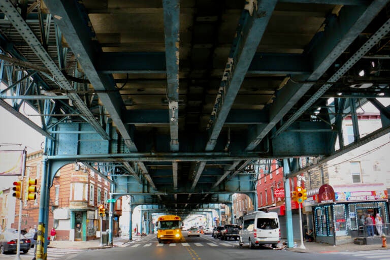 Cars drive on the street underneath the elevated train tracks.