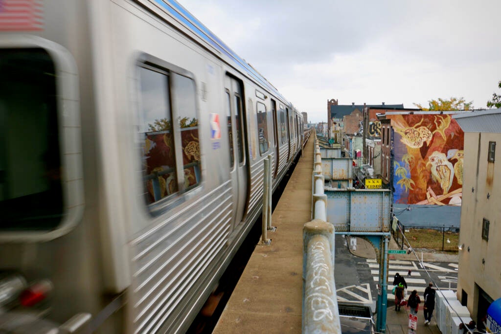 A train speeds by, buildings and a mural are visible in the lower right corner.