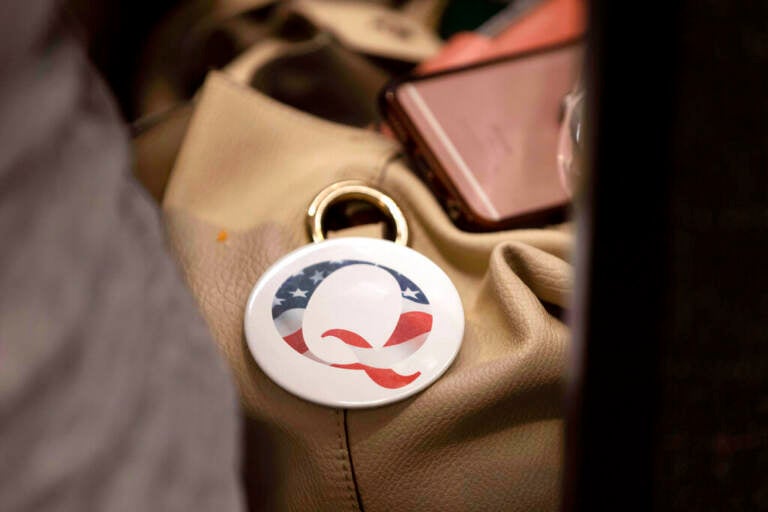 FILE - A QAnon conspiracy theory button sits affixed to the purse of an attendee of the Nebraska Election Integrity Forum on Saturday, Aug. 27, 2022, in Omaha, Neb. Former President Donald Trump is increasingly embracing and endorsing the QAnon conspiracy theory, even as the number of frightening real-world incidents linked to the movement increase. On Tuesday, Sept. 13, 2022, using his Truth Social platform, Trump reposted an image of himself — wearing a Q lapel pin — overlaid with the words “The Storm is Coming.