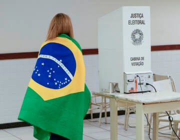 A voter wrapped in a Brazilian flag arrives to vote in a presidential a run-off pitting President Jair Bolsonaro against former President Luiz Inácio Lula da Silva, in Brasilia, Brazil, Sunday, Oct. 30, 2022. (AP Photo/Eraldo Peres)