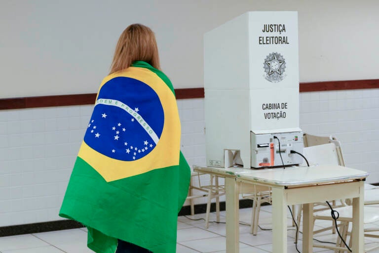 A voter wrapped in a Brazilian flag arrives to vote in a presidential a run-off pitting President Jair Bolsonaro against former President Luiz Inácio Lula da Silva, in Brasilia, Brazil, Sunday, Oct. 30, 2022. (AP Photo/Eraldo Peres)