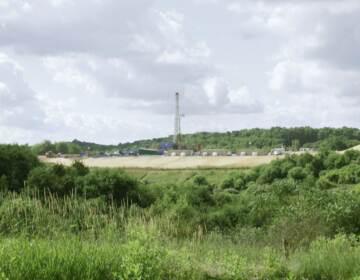 A green landscape is visible with a drilling rig in the background.