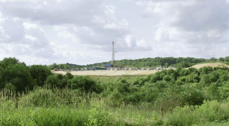 A green landscape is visible with a drilling rig in the background.