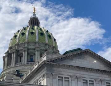 The green dome of the Harrisburg State Capitol building is visible against a blue sky and clouds.