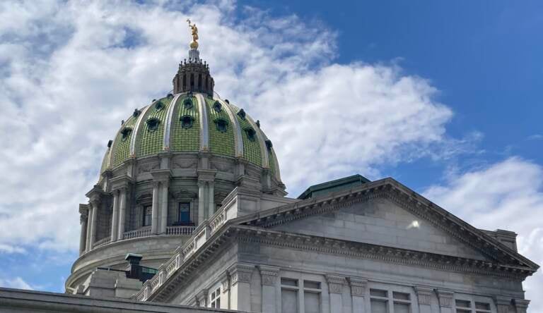 The green dome of the Harrisburg State Capitol building is visible against a blue sky and clouds.