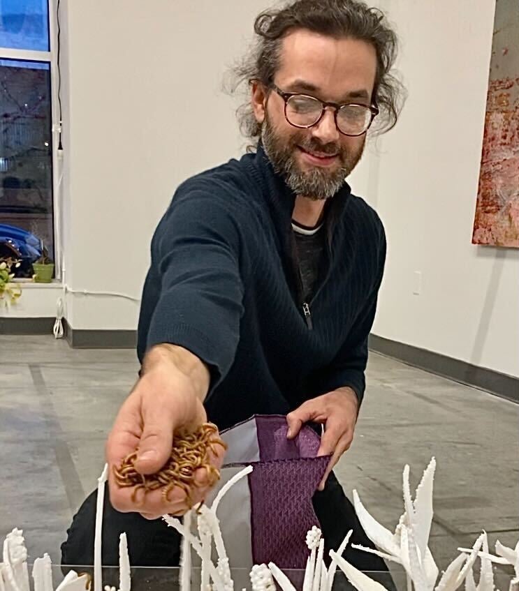 A man reaches toward a Styrofoam sculpture with a hand full of worms.