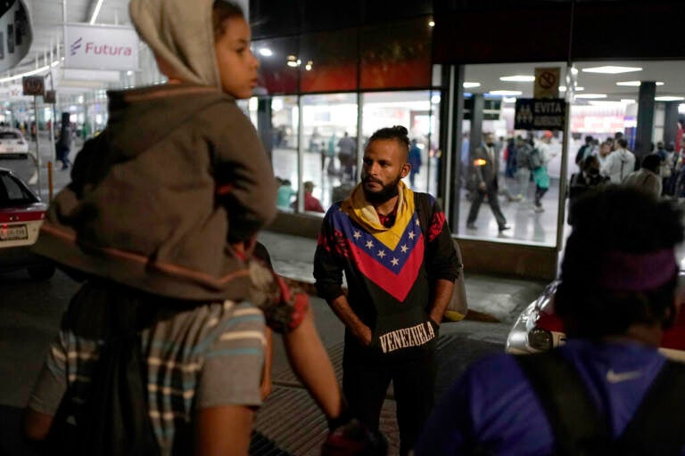 A man group of people stand together, waiting for a bus.