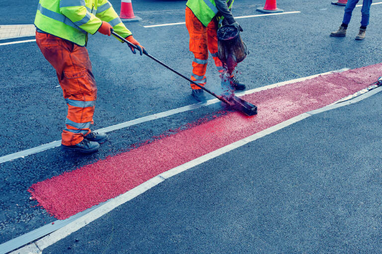 Road workers applying hot red road marking paint on new build road