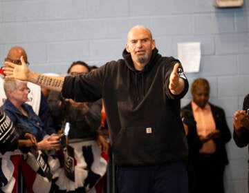 John Fetterman gestures with his arms while speaking as people look on.