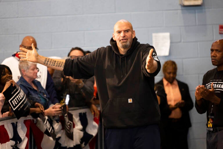 John Fetterman gestures with his arms while speaking as people look on.