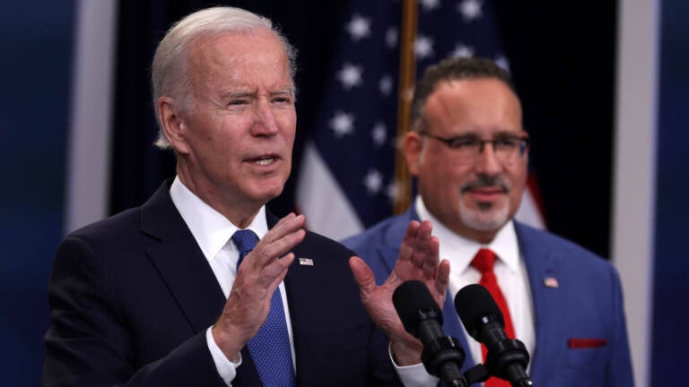 President Joe Biden speaks on the student debt relief plan as Secretary of Education Miguel Cardona (right) listens