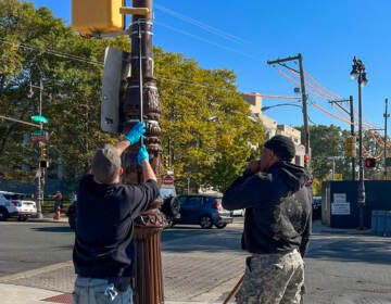 City workers grease a light pole on a sunny day.