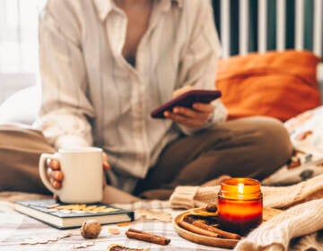 An up-close view of a person sitting in bed, holding a coffee mug, with a candle lit in front of them.