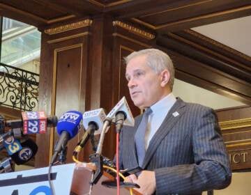 Krasner stands at a podium and speaks into microphones from various media outlets.