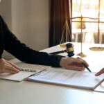 A lawyer points to something on a document. The hand of the person seated across the table from her is visible.