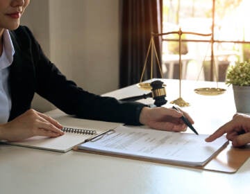 A lawyer points to something on a document. The hand of the person seated across the table from her is visible.