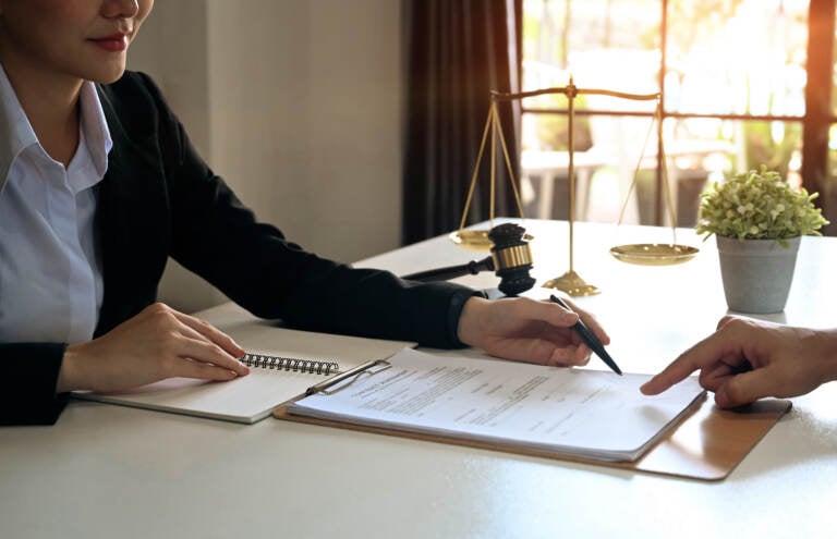 A lawyer points to something on a document. The hand of the person seated across the table from her is visible.