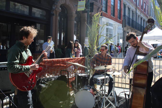 A band plays guitar, drums, and cello on the street.