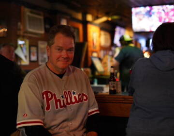 A man wearing a Phillies jersey sits at a bar.