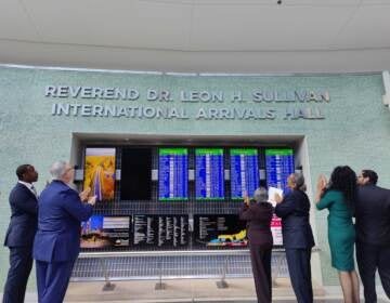 Mayor Jim Kenney (in blue) and Mable Ellis Welborn (in maroon), board chair of the Leon H. Sullivan Charitable Trust, unveil the new name of the international arrivals hall at the Philadelphia airport. (Peter Crimmins/WHYY)