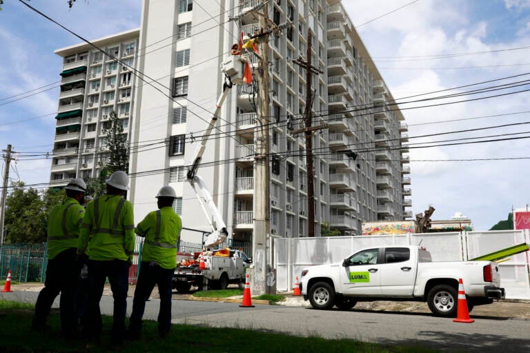 Workers repair an electrical wire in front of a tall building.
