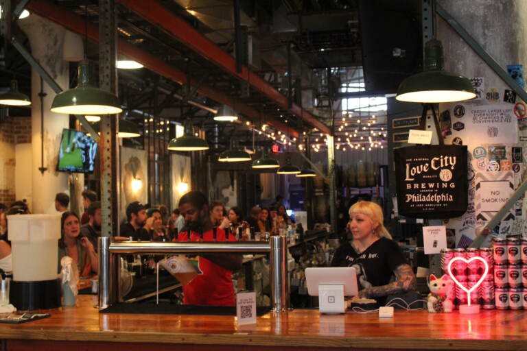 People gather around a bar. A sign reads Love City Brewing.