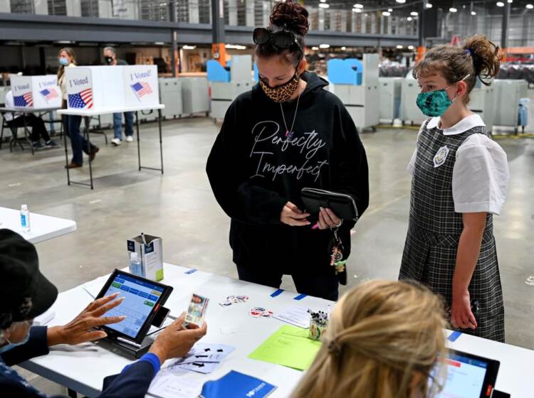 Dos personas están al lado de una mesa donde están sentados dos personas con computadoras.