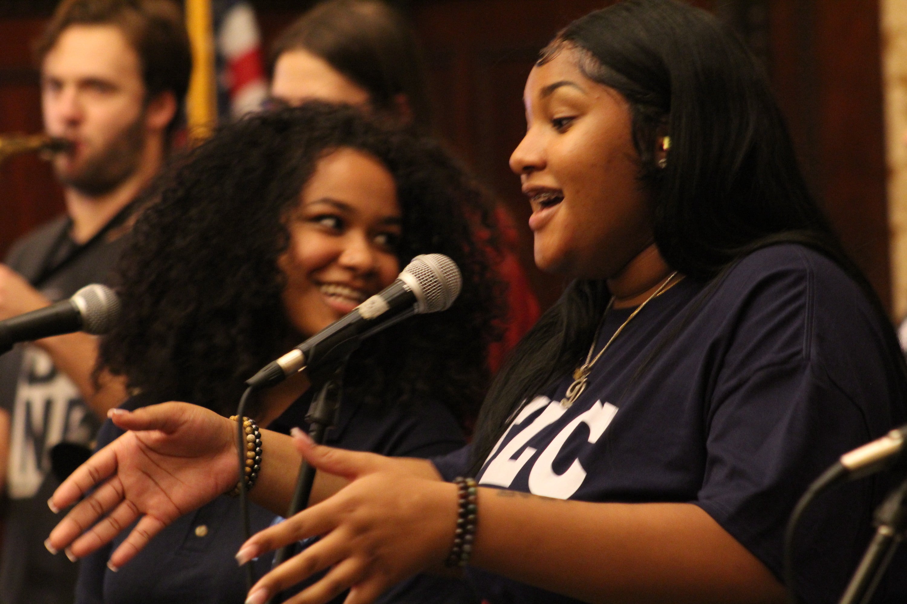 A person sings into a microphone as musicians play behind her.