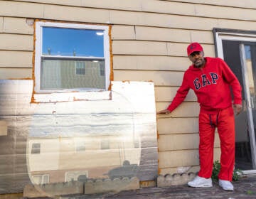 Lemuel Bannister estimates the height of the flooding caused by Isais in 2020. Holes along the bottom of the siding are covered up with an insulation board to keep his pipes from freezing in the winter. (Kimberly Paynter/WHYY)