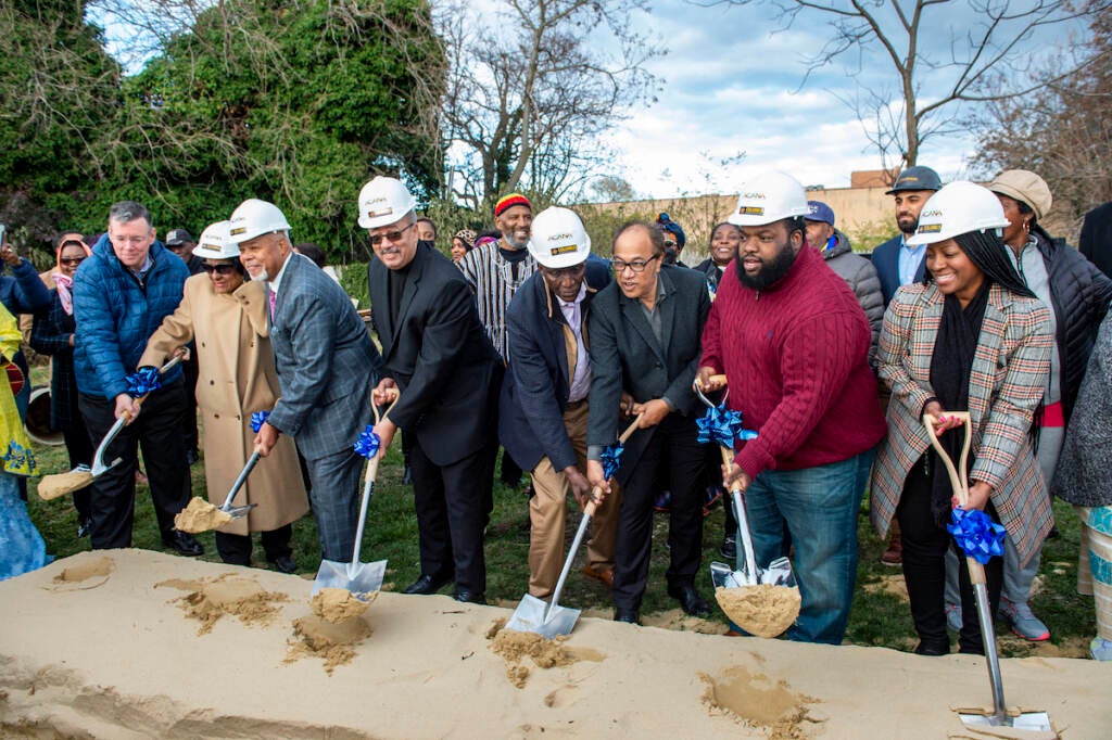 People hold shovels and break ground at a ceremonial opening.