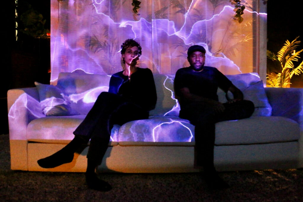 Two people sit on a couch with purple lights flowing over them.