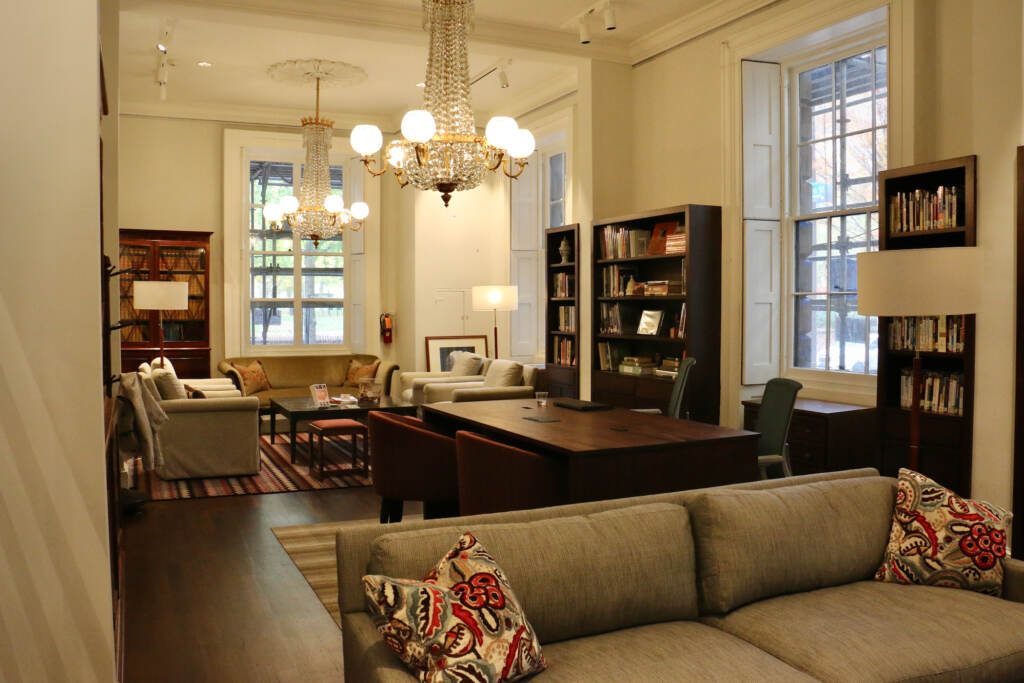 A room is lit with warm lighting. Couches, tables and bookshelves are visible.